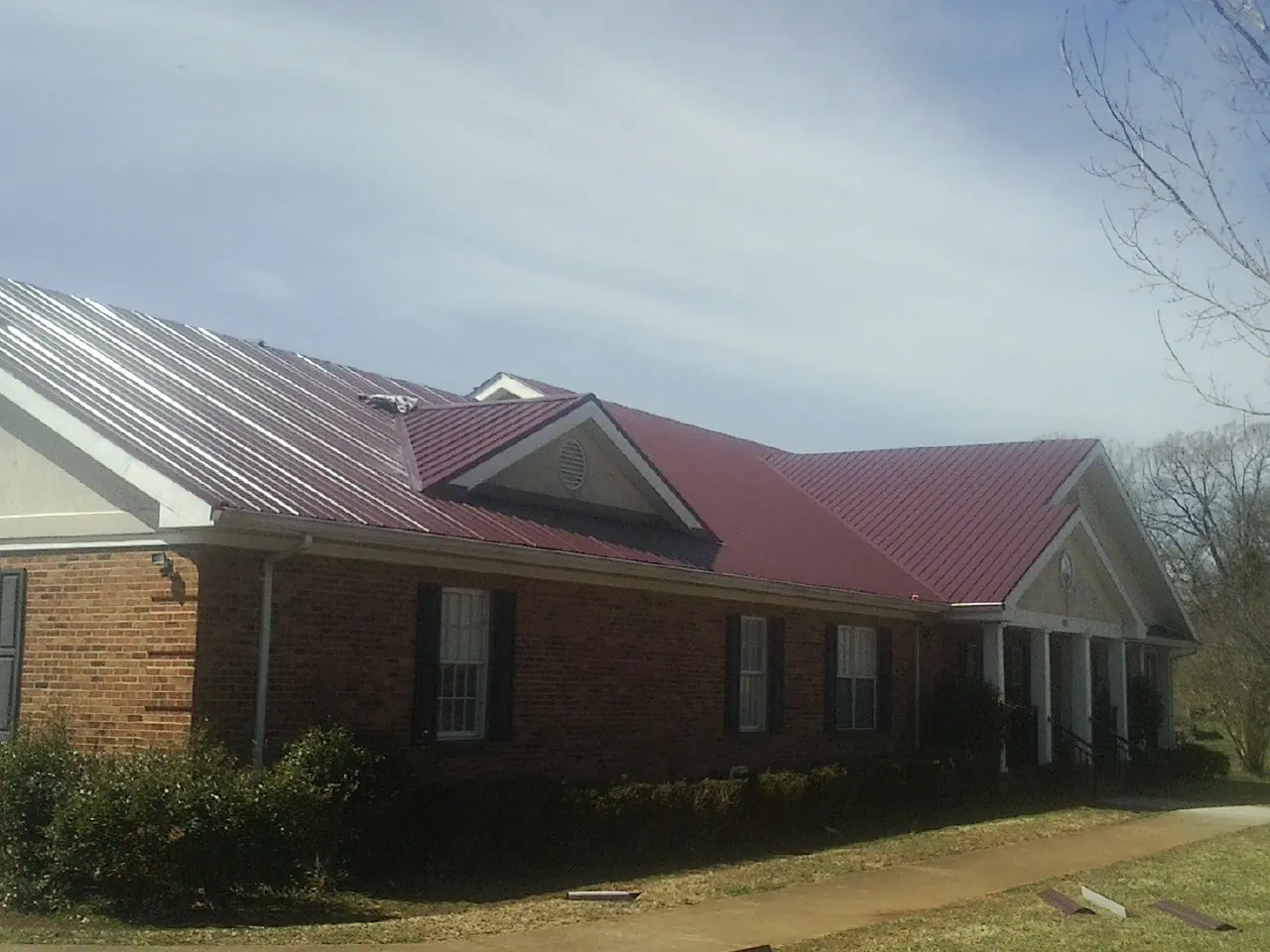 Red metal roof with gabled entries on a long brick building, from a Hail Damage Roof Repair job in Maysville