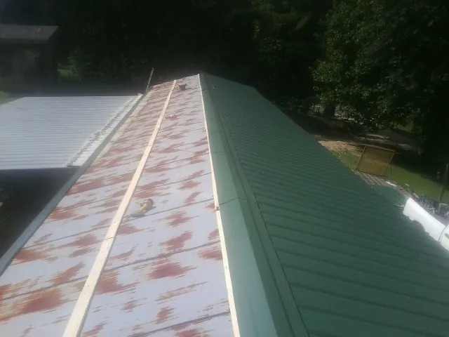 Old rusted panels beside newly installed green metal roofing — Wind Damage Roof Repair by Roofing Brothers in Maysville