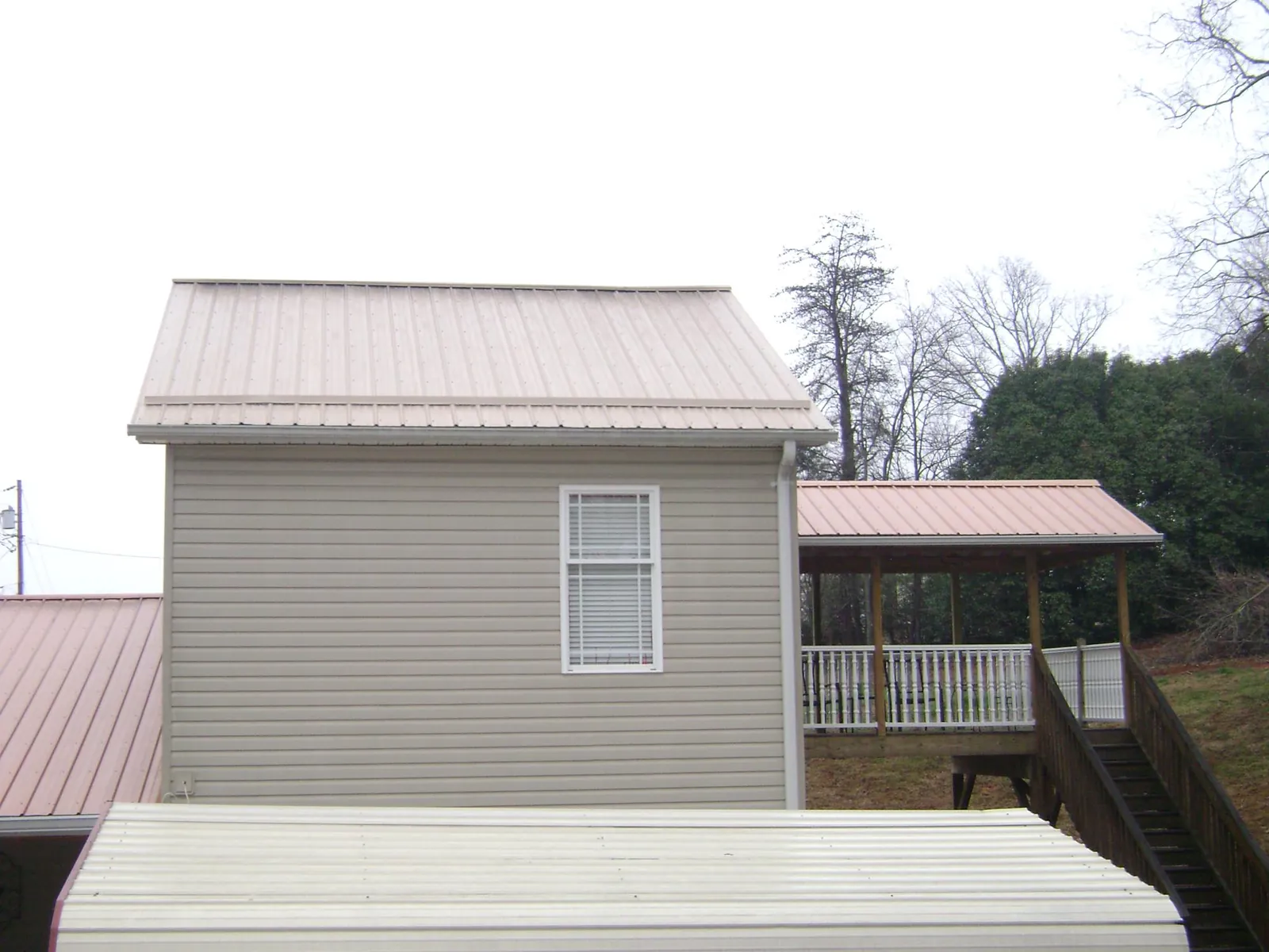 Tan metal roofs on a two story addition and attached porch, from a Roof Replacement job in Maysville